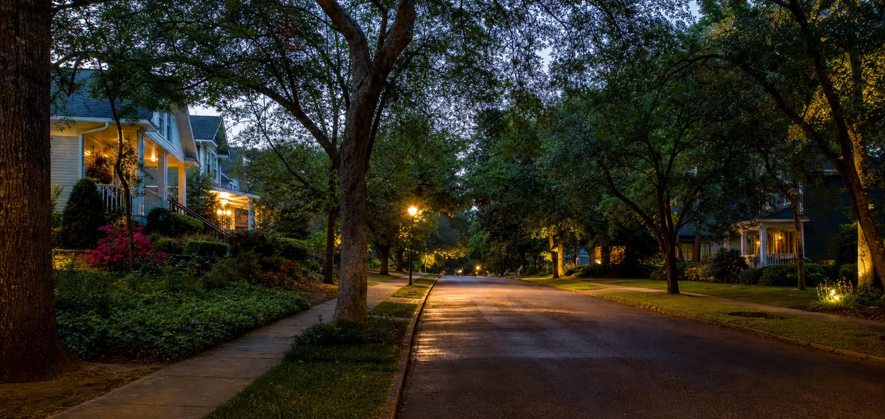 Quiet tree-lined residential street in a Georgia suburb at dusk with porch lights glowing